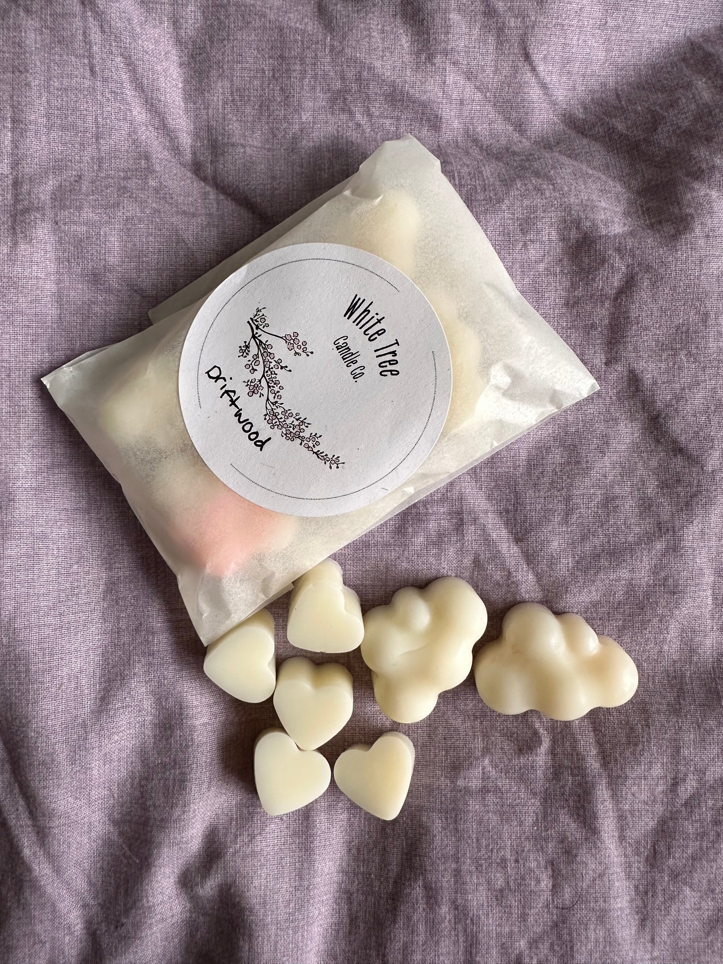 Heart and cloud-shaped homemade soy wax candles on a purple fabric background.