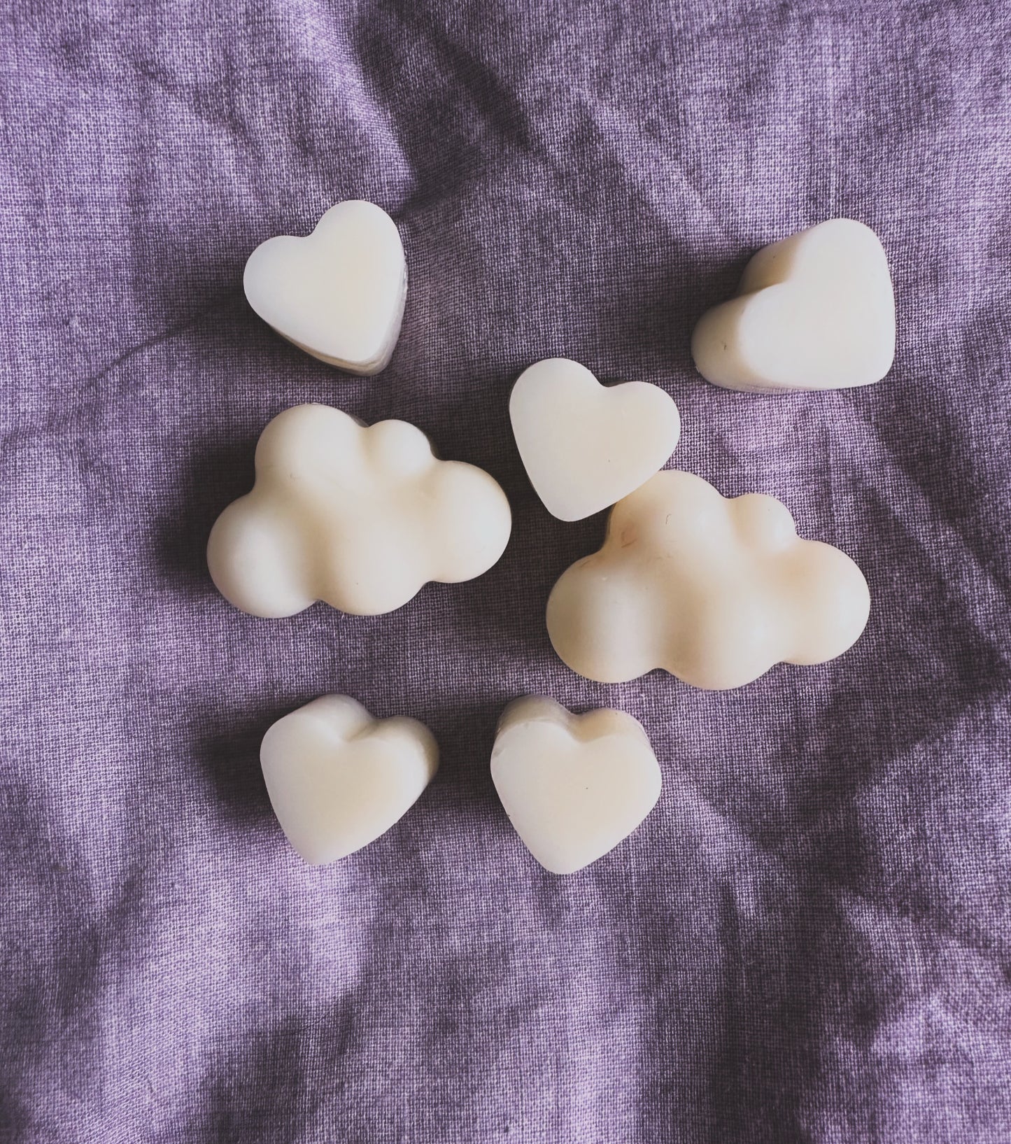 Heart and cloud-shaped homemade soy wax candles on a purple fabric background.