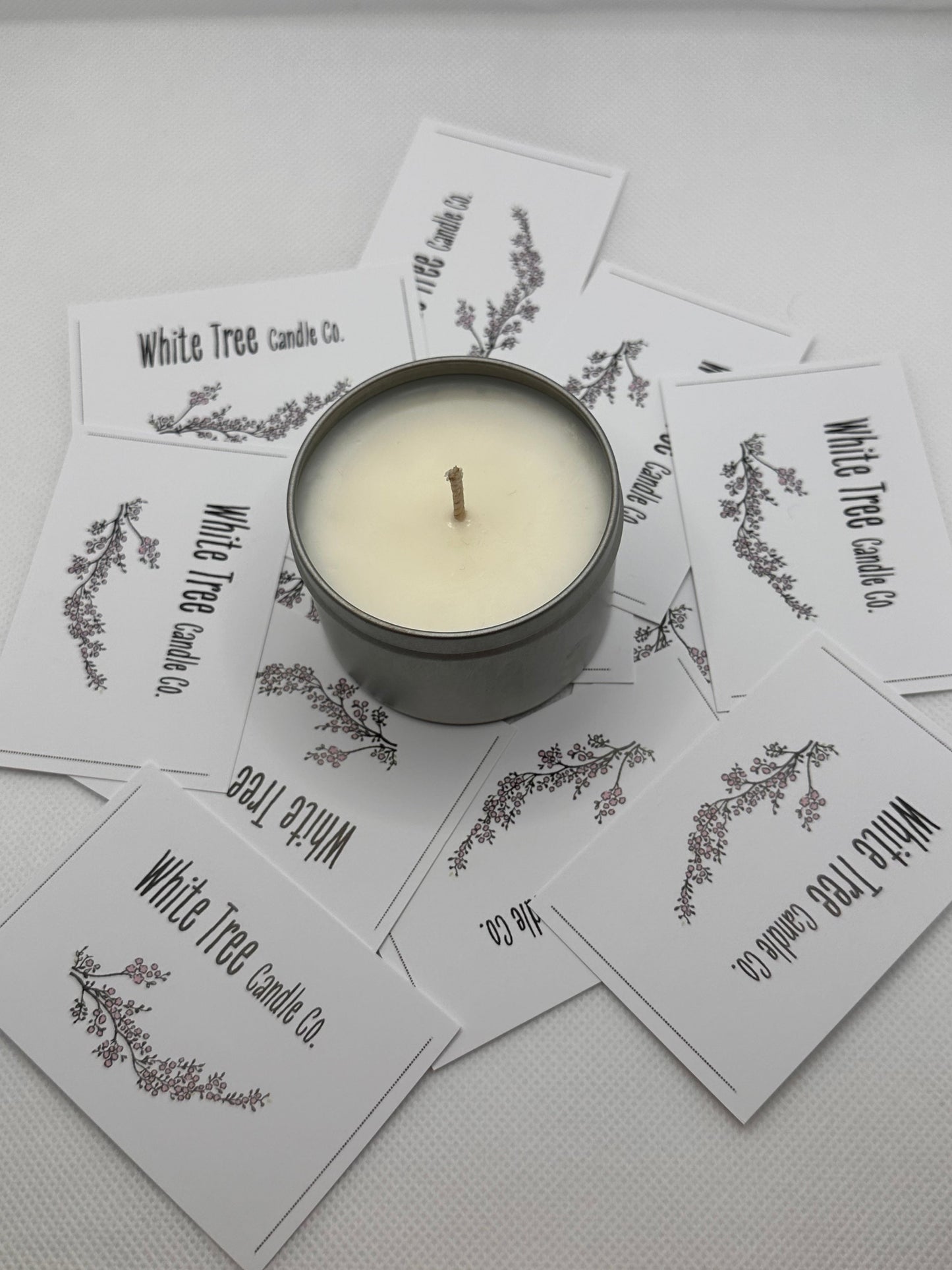 small hand poured candle in a silver tin on a white background with business cards